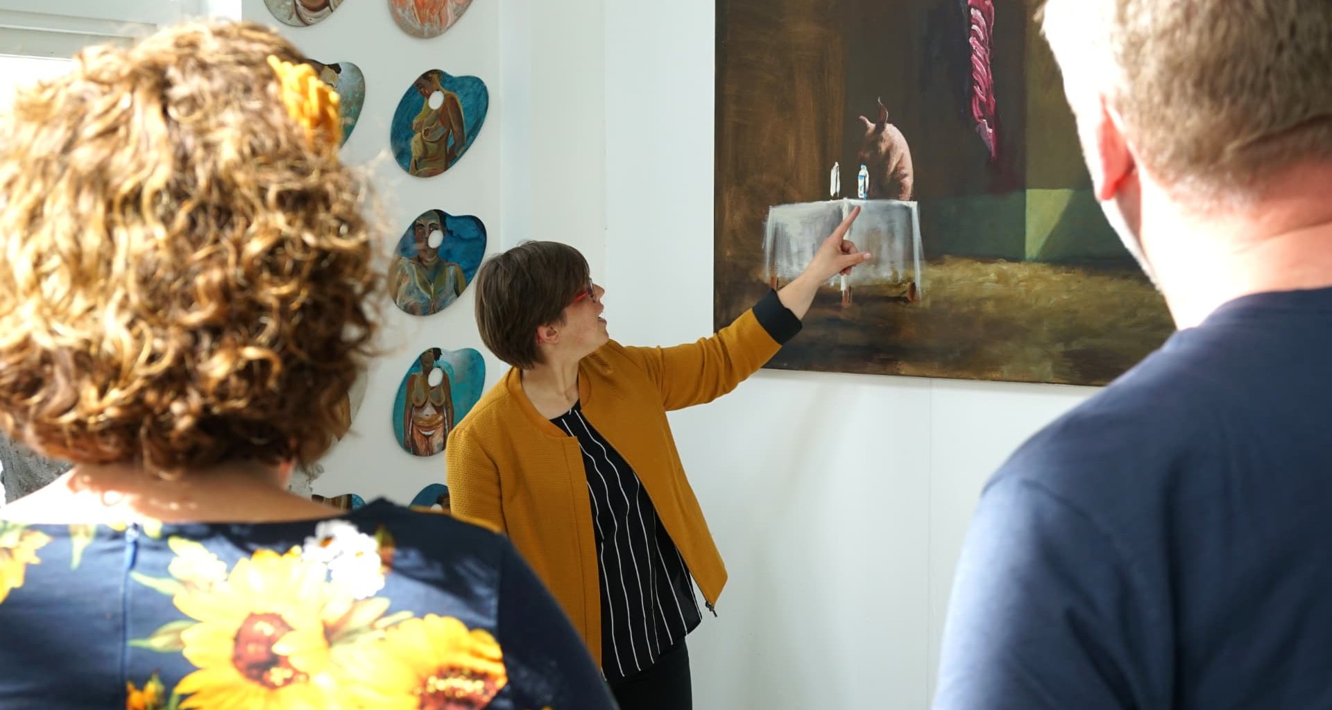 A museum guide pointing out details in a painting while two visitors look on
